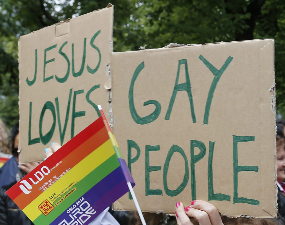 People hold a rainbow flag and signs saying "Jesus Loves Gay People" during a 2014 gay pride parade in Oslo, Norway.