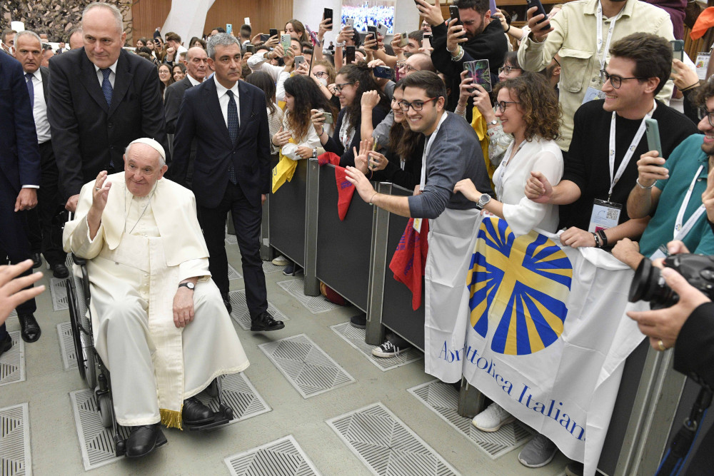 Pope Francis greets a crowd of people while sitting in a wheelchair
