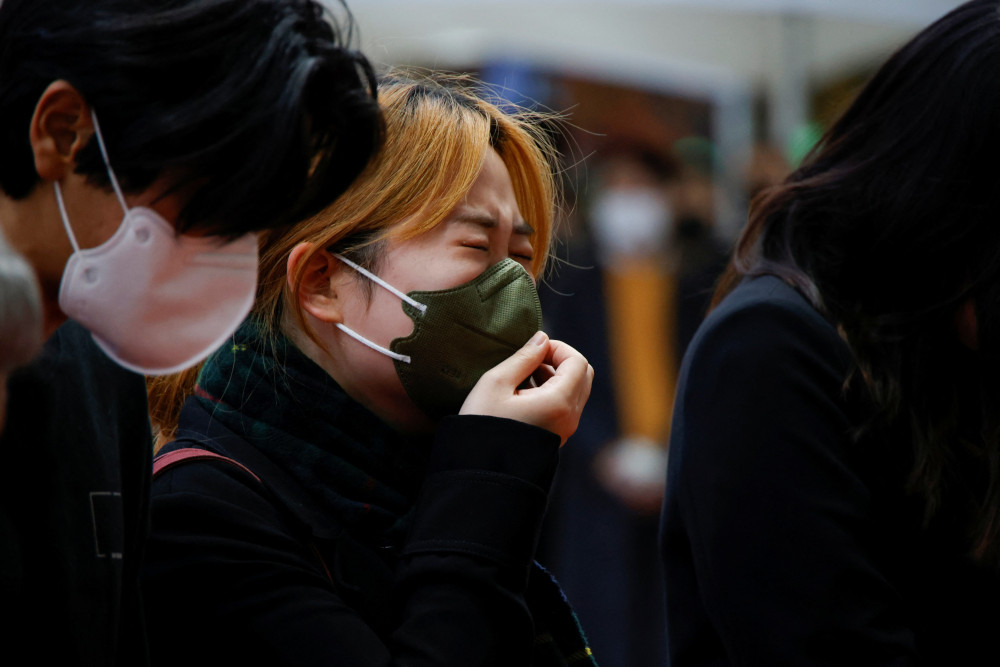 A South Korean woman wearing a mask cries beside another person wearing a mask
