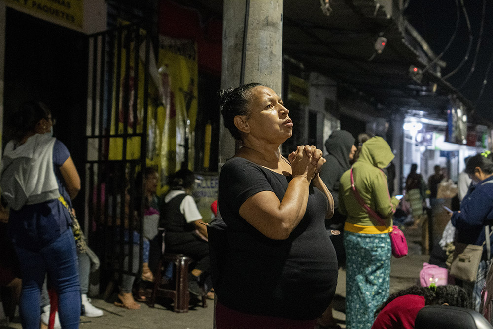 A woman prays as relatives wait for information about people arrested under the ongoing "state of exception," outside a detention center in San Salvador, El Salvador, Oct. 11. (AP/Moises Castillo)