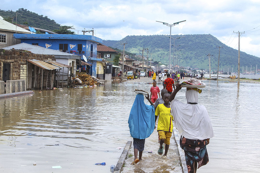 People walk through floodwaters following several days of downpours in Kogi, Nigeria, Oct. 6. Officials in Nigeria have called the floods the country's worst in more than a decade, blaming the disaster on heavy rainfall and the release of excess water from the Lagdo Dam in neighboring Cameroon. (AP/Fatai Campbell)