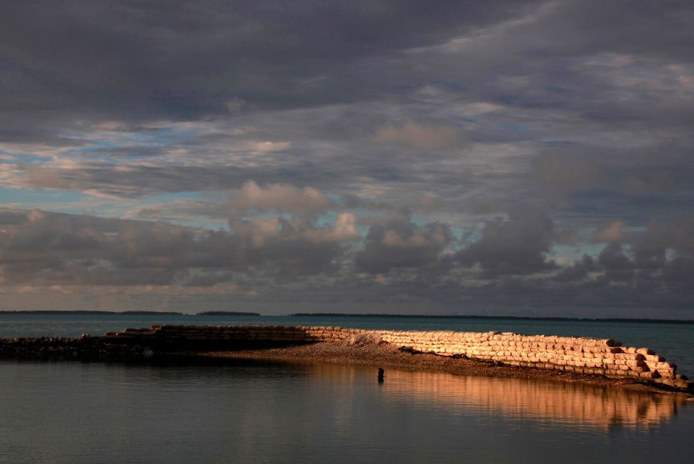 A man swims next to a manmade wall built to protect the island of South Tarawa from rising tides in the central Pacific island nation of Kiribati May 25, 2013. 