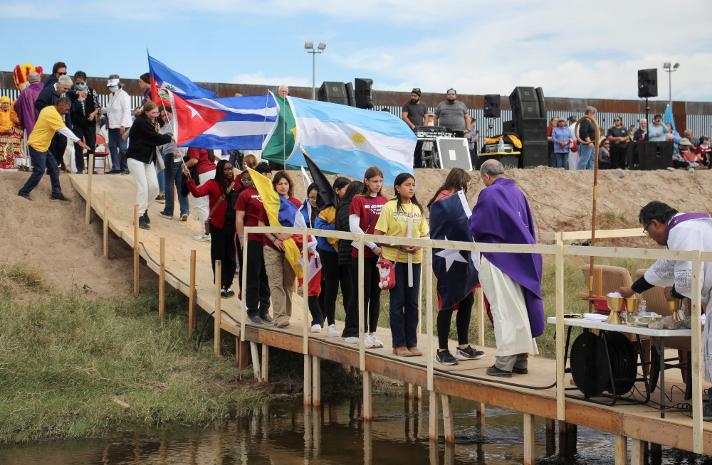 Migrants with flags line up on a bridge across the Rio Grande to receive communion from Bishop Mark Seitz 