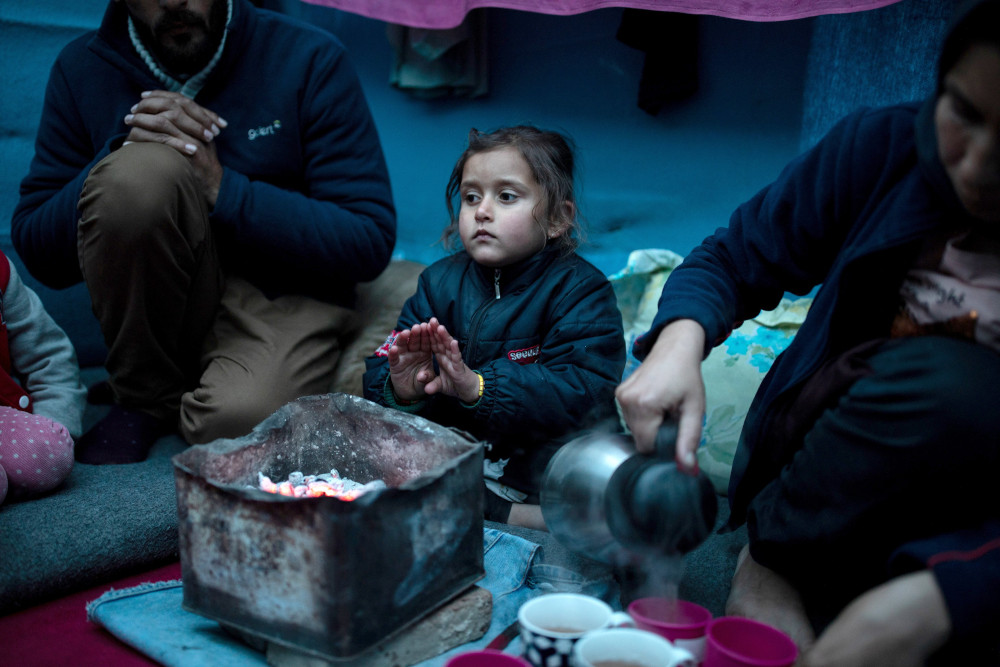 A girl is pictured in a file photo warming her hands over hot coal next to her parents inside their temporary shelter on the island of Lesbos, Greece. 