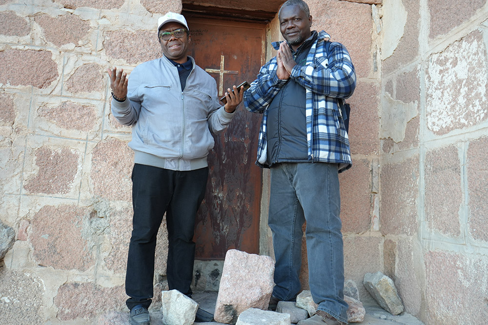 Frs. Vitalis Anaehobi, left, and Leonard Chiti stand at the peak of Mount Sinai Nov. 14, in front of a house where it’s believed the tablets with the Ten Commandments were kept. (EarthBeat photo/Doreen Ajiambo)