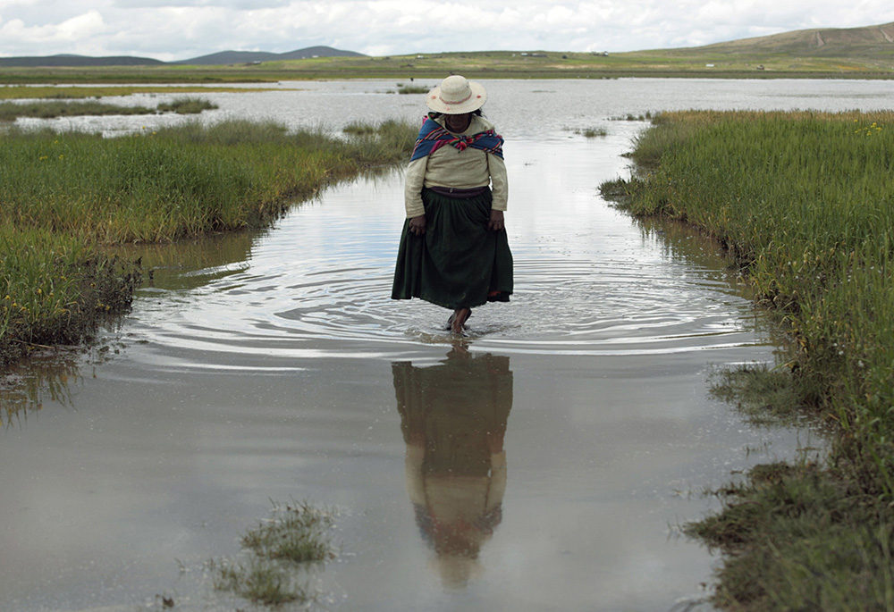 An indigenous woman is pictured in a file photo wading through floodwaters on a farm after heavy rains near La Paz, Bolivia. (CNS/Reuters/Gaston Brito)