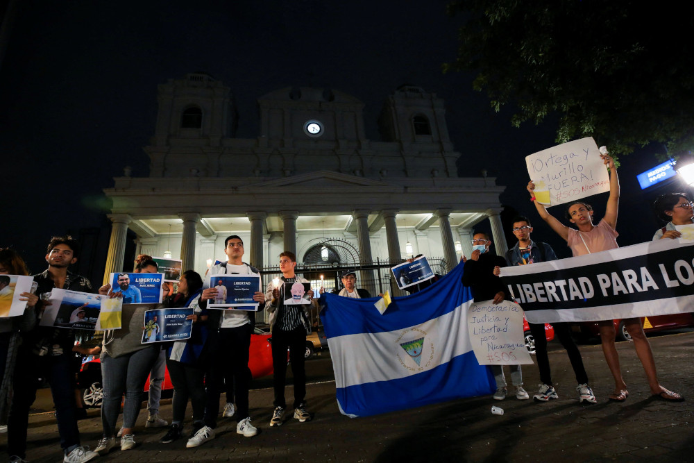People carry the Nicaraguan flag and protest signs outside a Cathedral in the dark