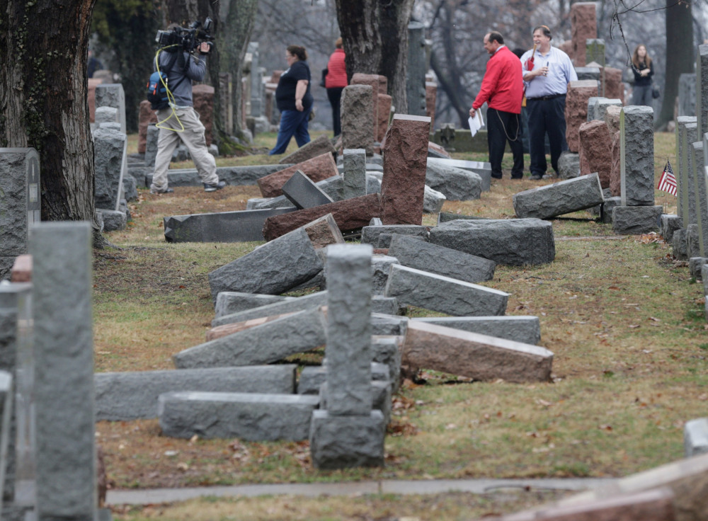 People walk in a cemetery full of toppled headstones