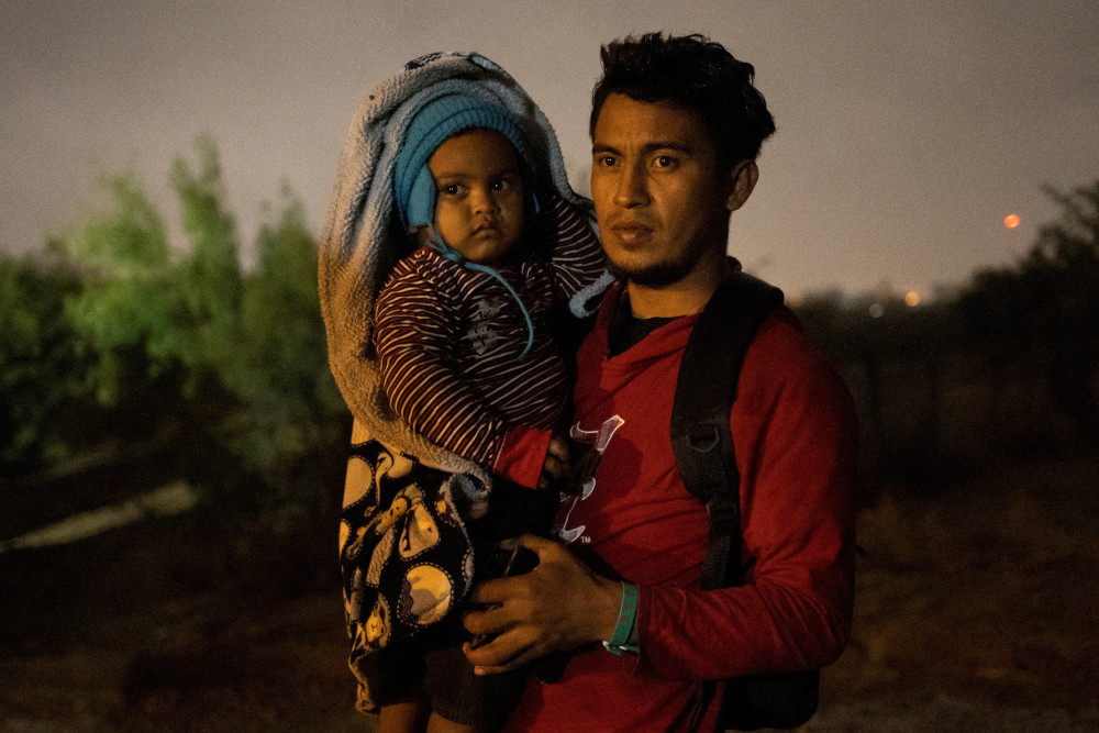 A man holds his small child who is bundled up for the cold night