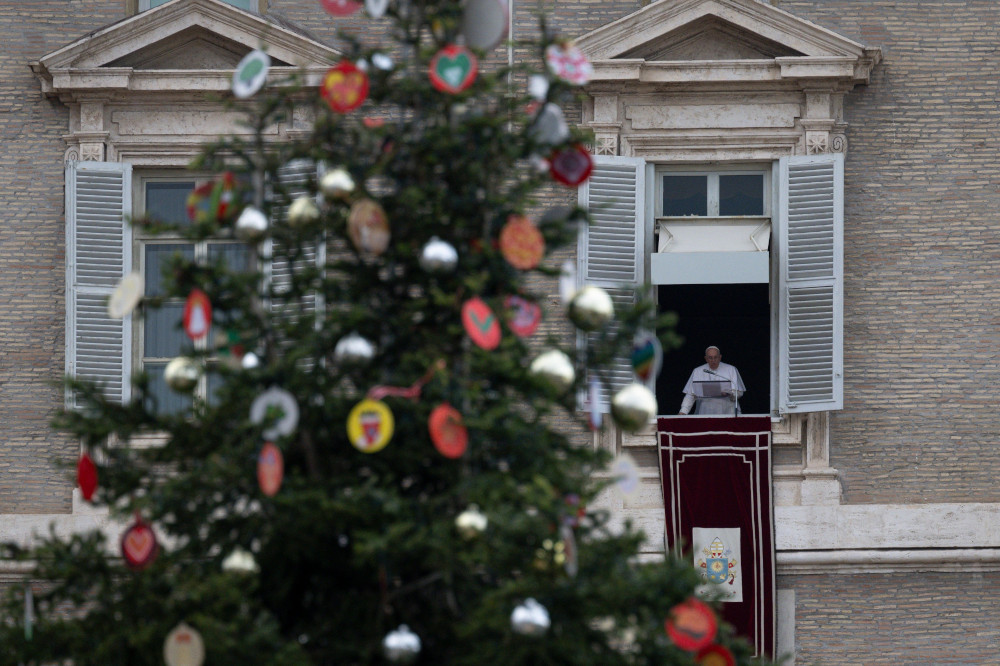 A Christmas tree stands in the foreground as Pope Francis appears in a Vatican window