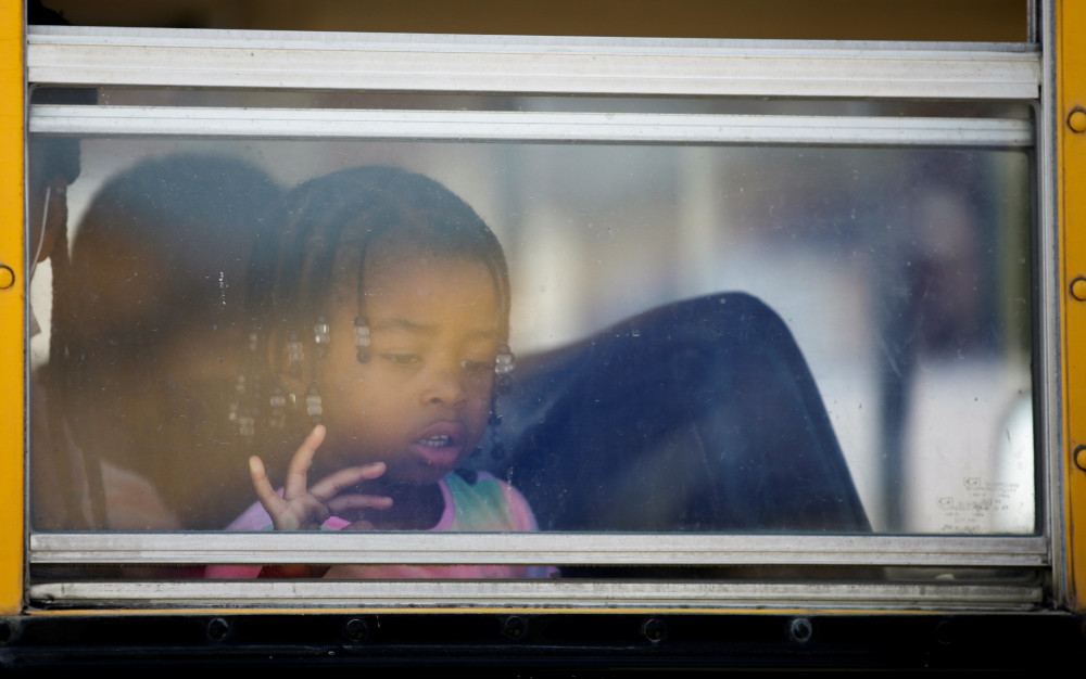 A young Black girl with braids looks out a school bus window