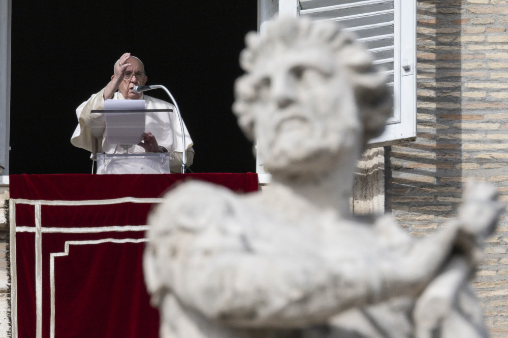 Pope Francis raises one hand over a podium with a piece of paper in the window of his apartment