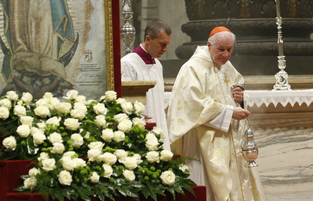 Cardinal Ouellet wears white vestments and stands next to a replicate tilma of Our Lady of Guadalupe