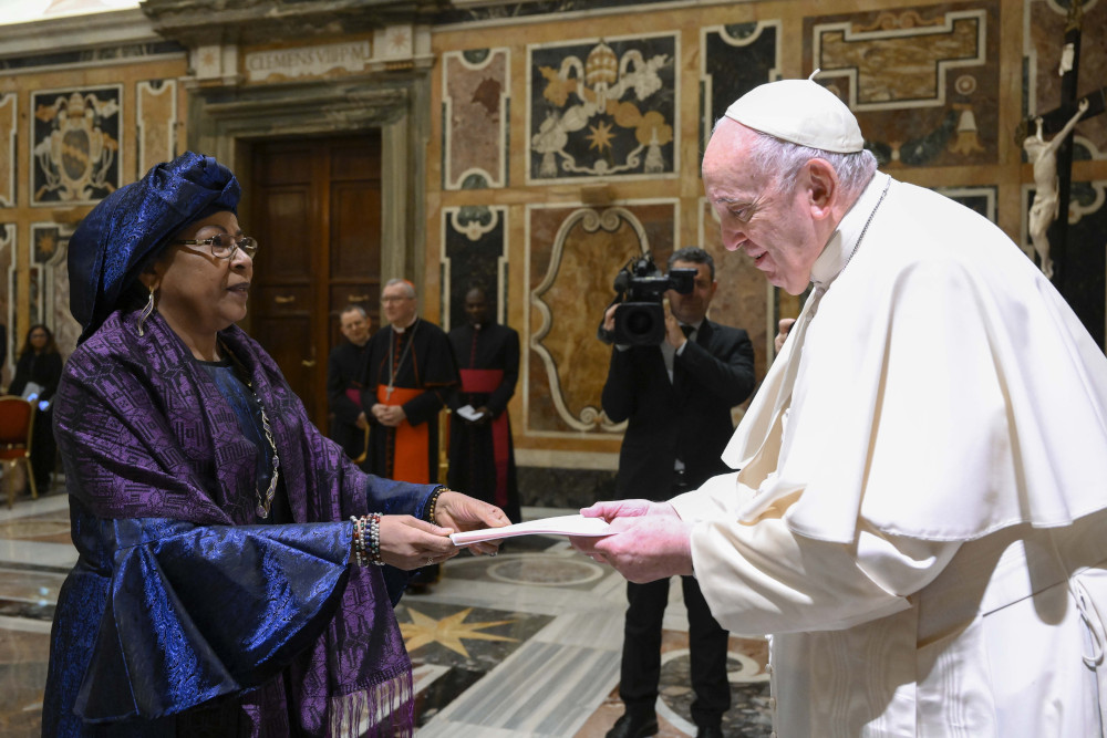 An elegantly dressed Black woman hands Pope Francis a letter