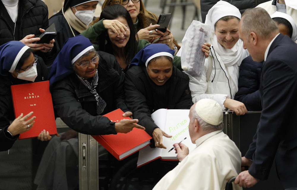 The pope signs a sister's red Bible as she stands among other sisters