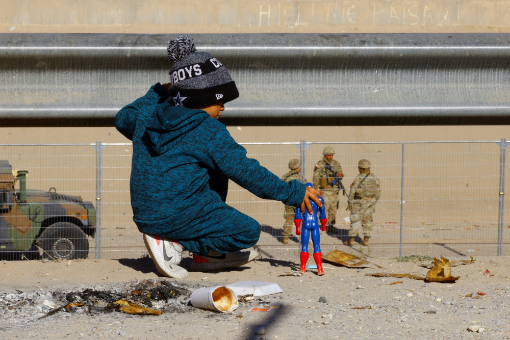 A child wearing a hat and coat plays with a Captain America figure in the desert