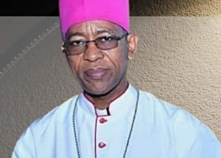 A Black man with glasses and a bishop's clothing looks at the camera