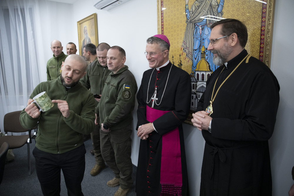 Archbishop Broglio speaks with men dressed in green military attire as another archbishop looks on