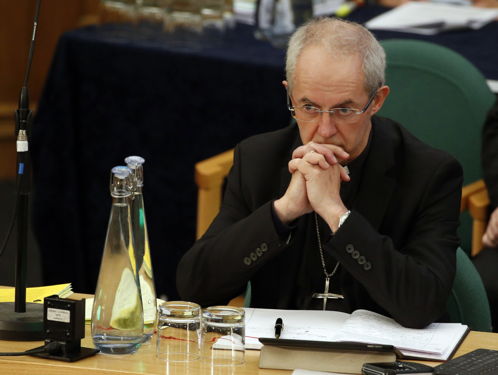 Justin Welby sits in a chair at a table with his hands folded in front of his face