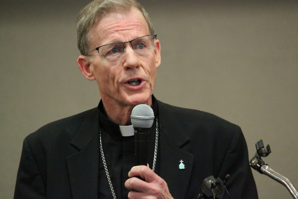 A white middle-aged bishop with glasses holds a microphone