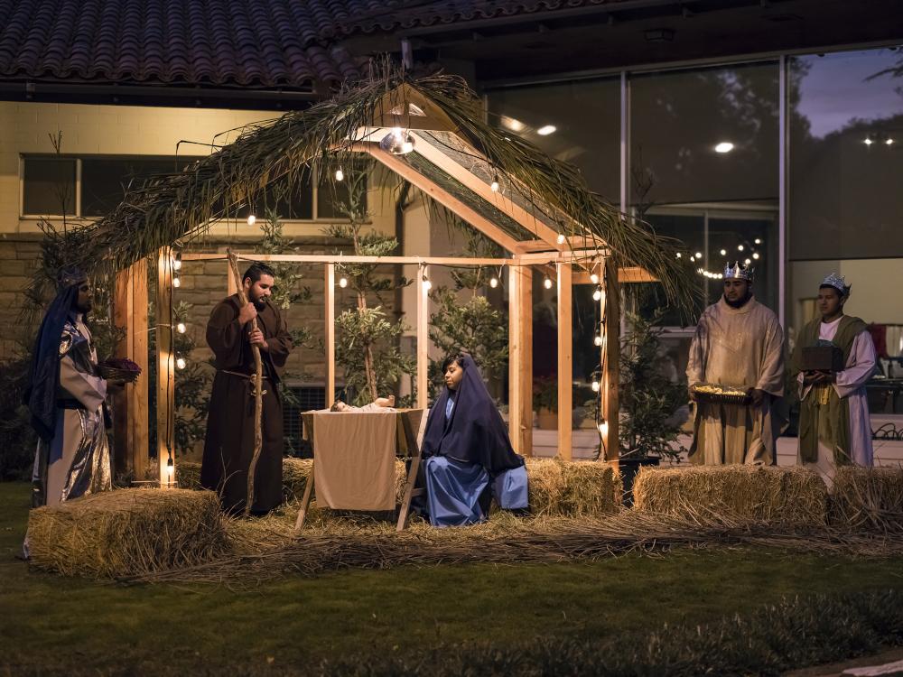 People sit in an outdoor nativity scene illuminated in the evening