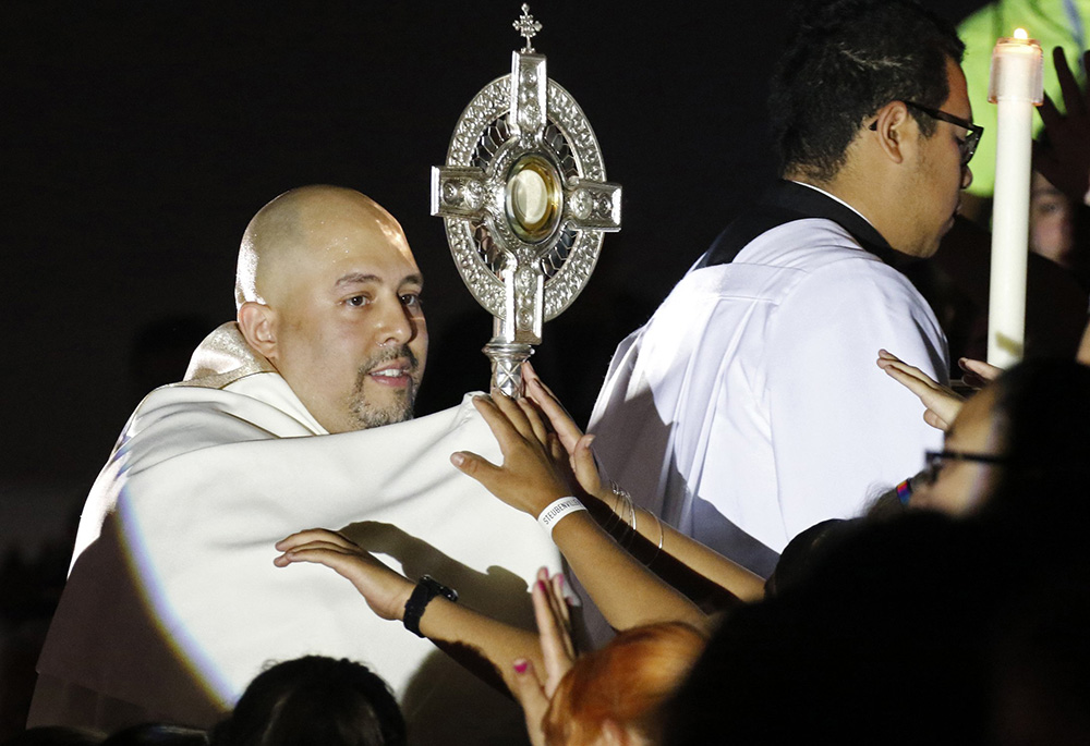 Fr. Joseph Espaillat carries a monstrance through the bleachers of Carnesecca Arena during eucharistic adoration at the Steubenville New York youth conference at St. John's University June 25, 2016, in Jamaica, New York. (CNS/Gregory A. Shemitz)