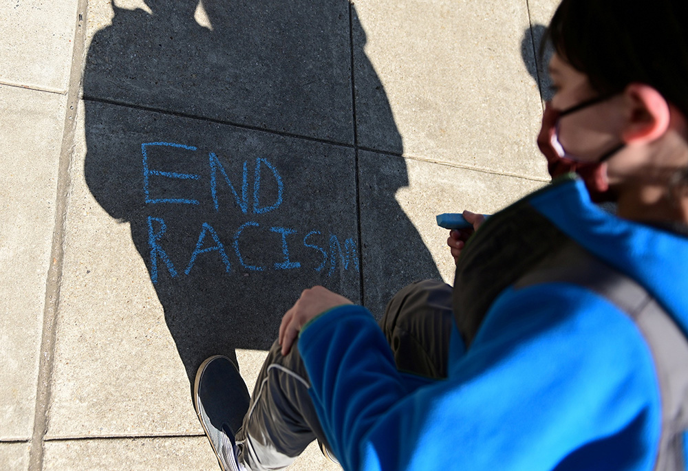 A child in Washington writes in chalk, "End racism," as people rally to protest recent violence against people of Asian descent March 21, 2021. (CNS/Reuters/Erin Scott)