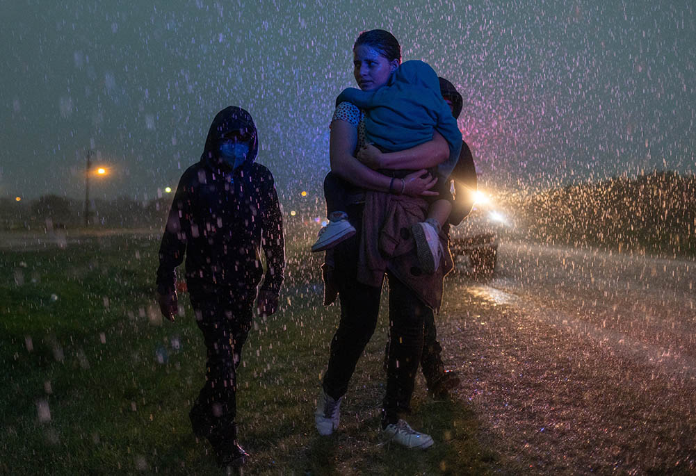 A mother from Central America and her three children are followed by a Texas Highway Patrol officer in La Joya, Texas, May 19, 2021, as they look for cover during a heavy rainfall after crossing the Rio Grande into the United States from Mexico. (CNS)