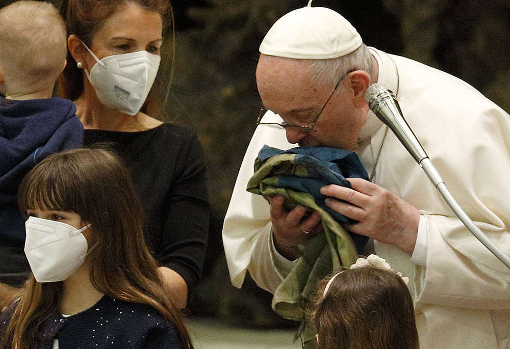 Pope Francis kisses a Ukrainian national flag from Bucha as he meets Ukrainian refugees during his general audience in the Paul VI hall April 6 at the Vatican. (CNS/Paul Haring)