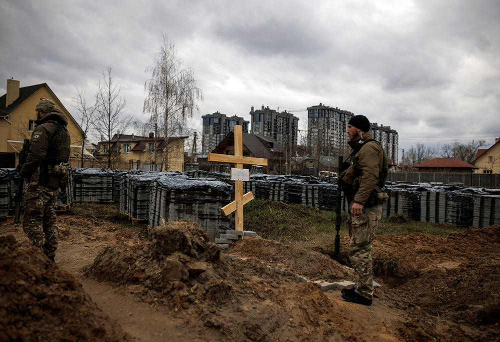 Ukrainian soldiers stand next to the grave of a civilian April 6 in Bucha, Ukraine. Local residents said the civilian was killed by Russian soldiers during Russia's invasion of Ukraine. (CNS/Reuters/Alkis Konstantinidis)