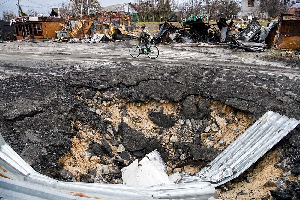 A local resident rides a bicycle past a bomb crater as Russia's attack on Ukraine continues in the village of Demydiv, outside Kyiv, Ukraine, April 6. (CNS/Reuters/Vladyslav Musiienko)