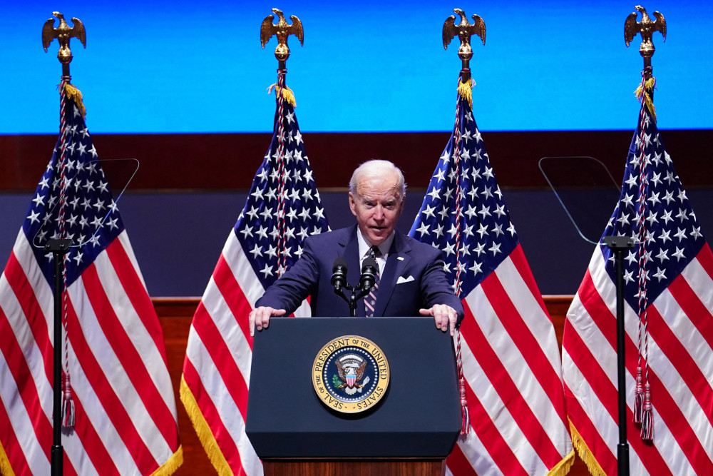 Biden stands behind a podium and in front of four American flags