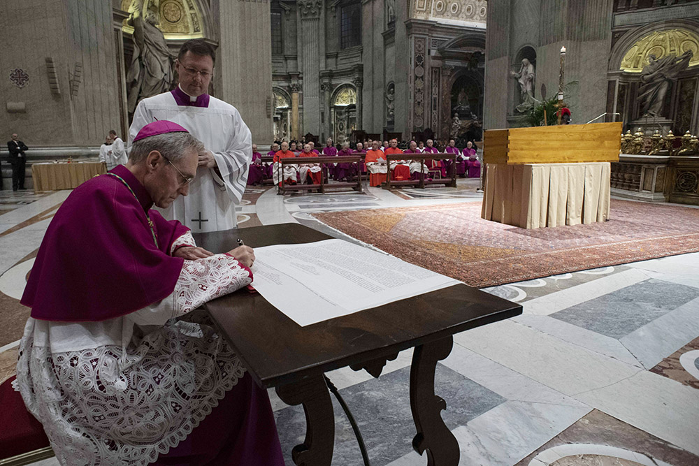 Archbishop Georg Gänswein, private secretary to Pope Benedict, signs a scroll known as a rogito to place with the body of Pope Benedict XVI in his cypress casket in St. Peter's Basilica at the Vatican Jan. 4. In addition to containing his biography, the legal document, written in Latin, also attested to his death and burial. (CNS/Vatican Media)