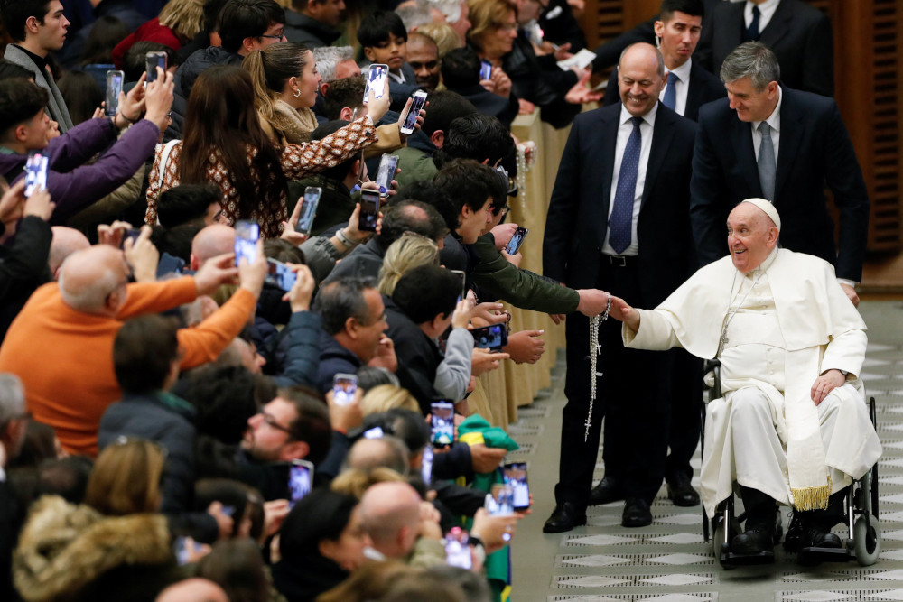 Pope Francis, with a big smile, wheels past an excited audience where people hold their cellphones up
