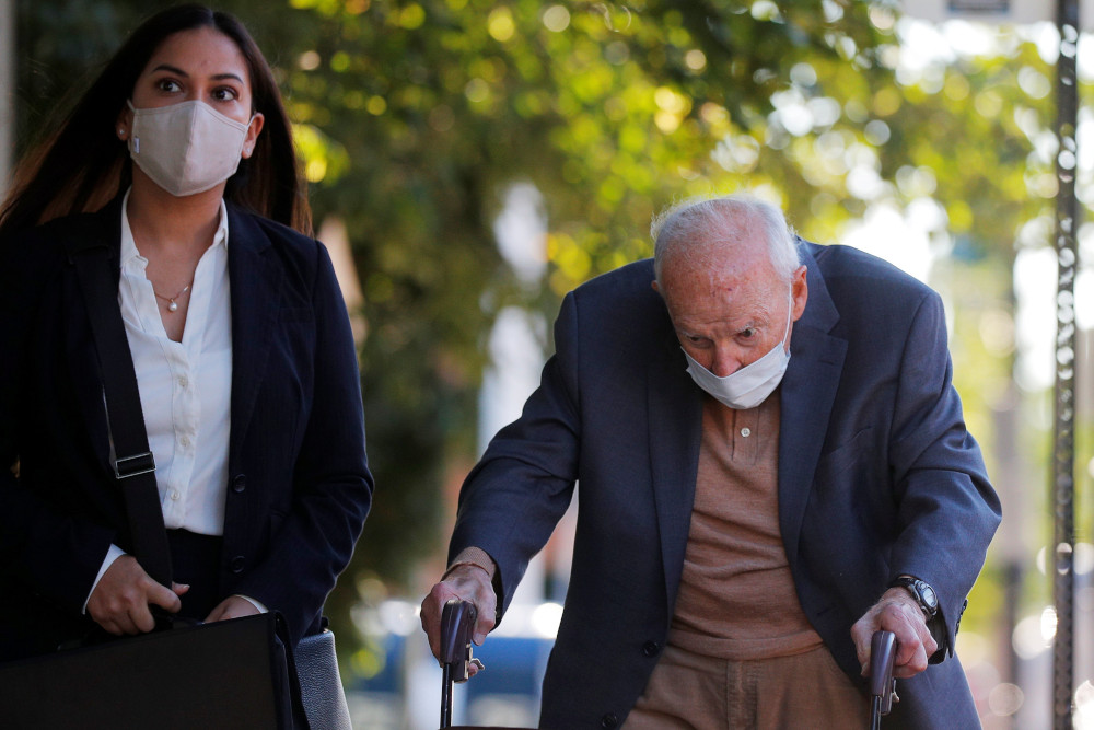 McCarrick wears a suit and suit and hunches over a walker. A young woman wearing a mask stands next to him.