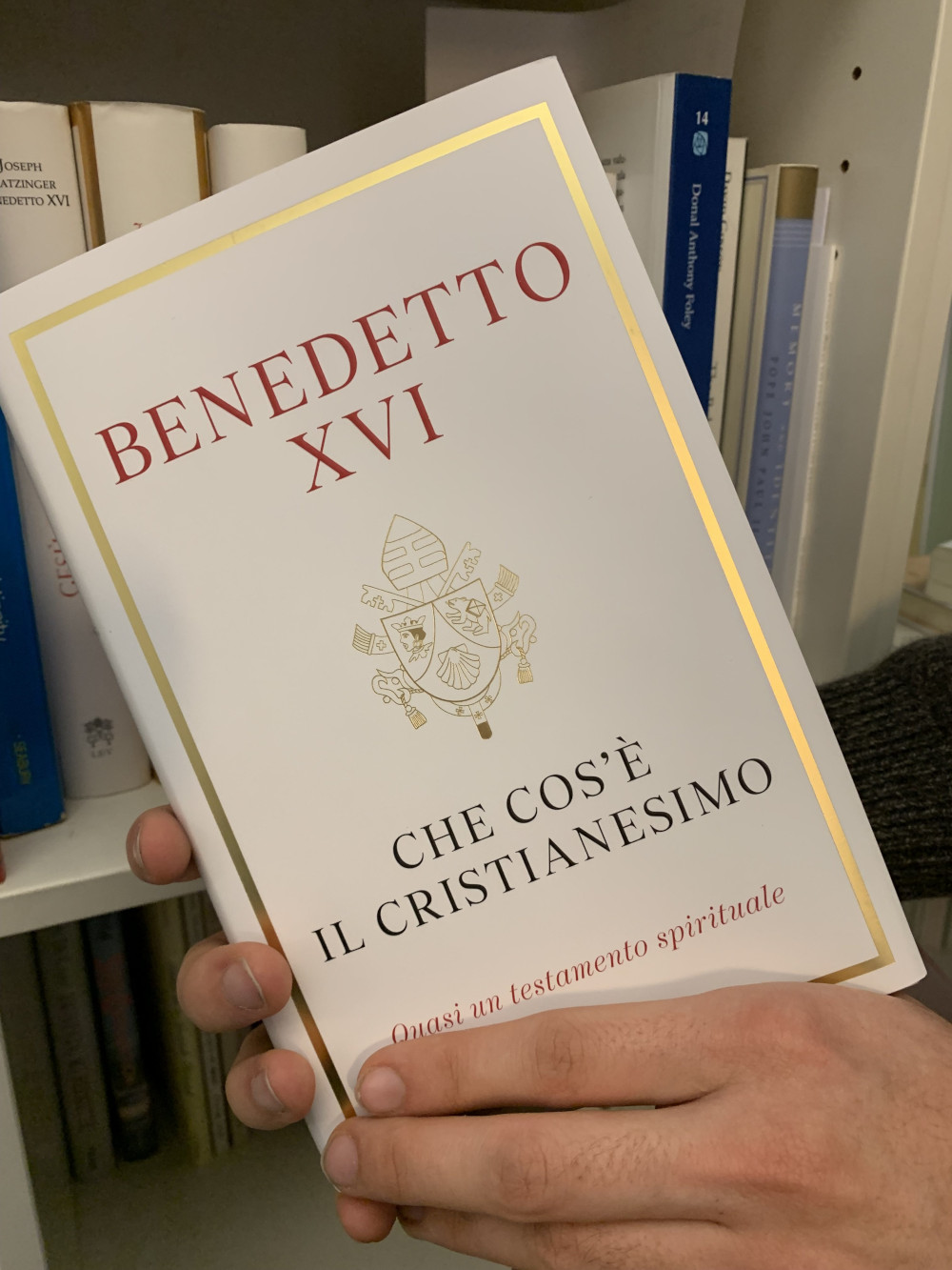 Hands hold up the book "Benedetto XI: Che cos'e il Cristanesmio" with a white and gold cover