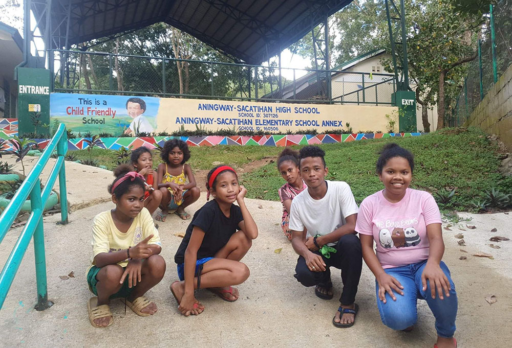 Jolina Tablan (in pink), Aeta Resettlement and Rehabilitation Center coordinator, and students pose for a photo at Aningway-Sacatihan High School and Aningway-Sacatihan Elementary School Annex in Subic, Zambales, Philippines. (Oliver Samson)