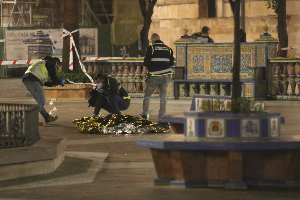 Police kneel and stand around a gold emergency blanket in the middle of a colorful plaza