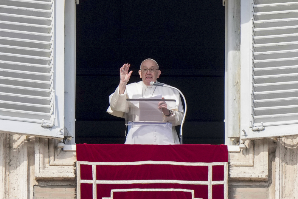 Pope Francis raises his hand as he stands behind a lectern in his window overlooking St. Peter's Square