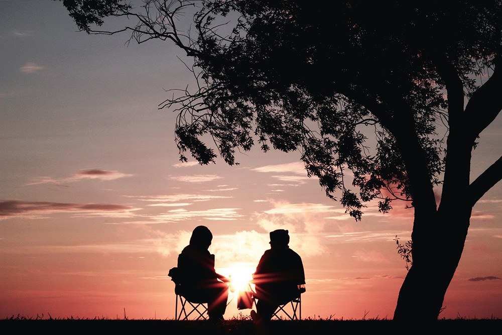 Two people seated outside, watching a sunset (Unsplash/Harli Marten)