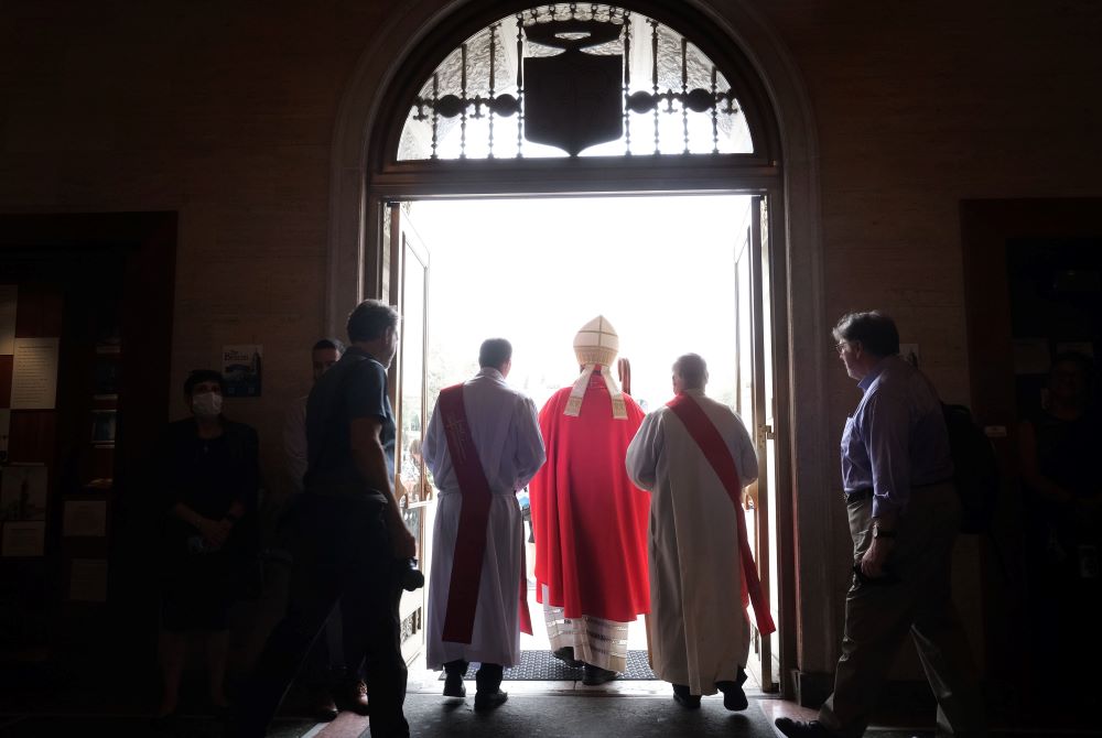 Cardinal is shown exiting a church, flanked by clergy.