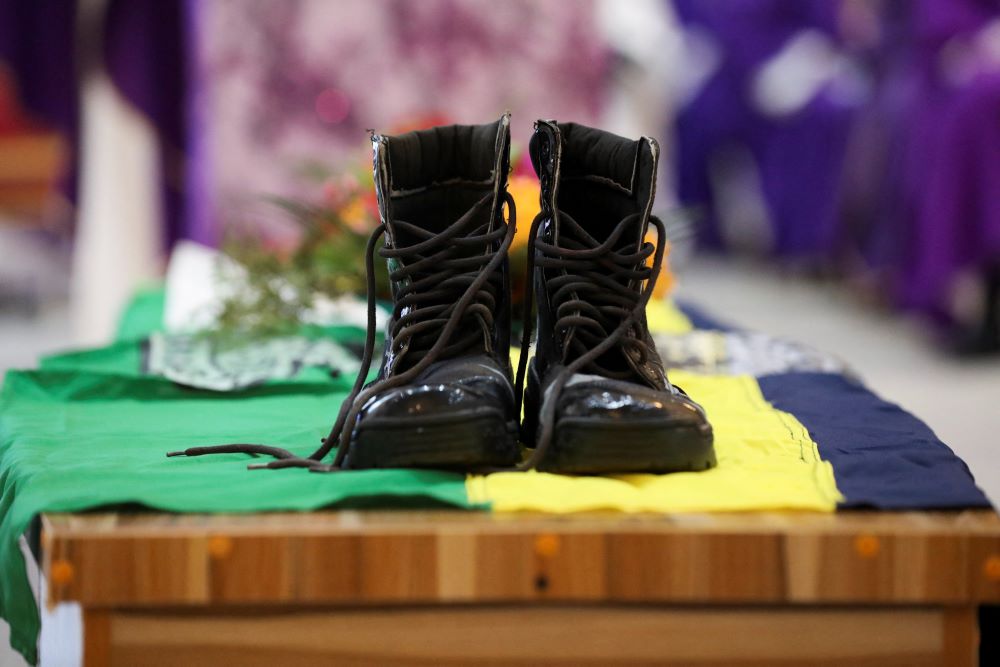 Black work boots sit atop a Nigerian flag, which is draped over a coffin.