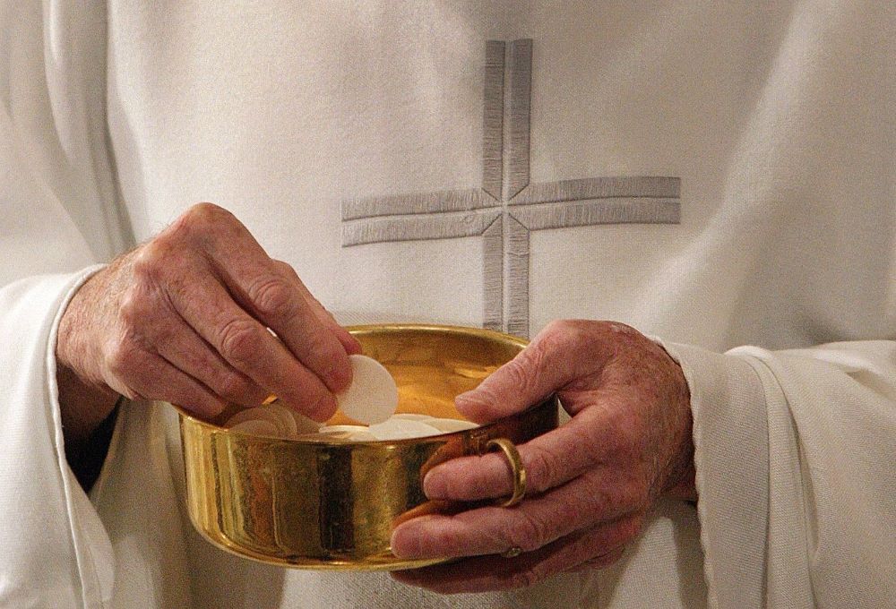 A priest holds bowl with Communion wafers.