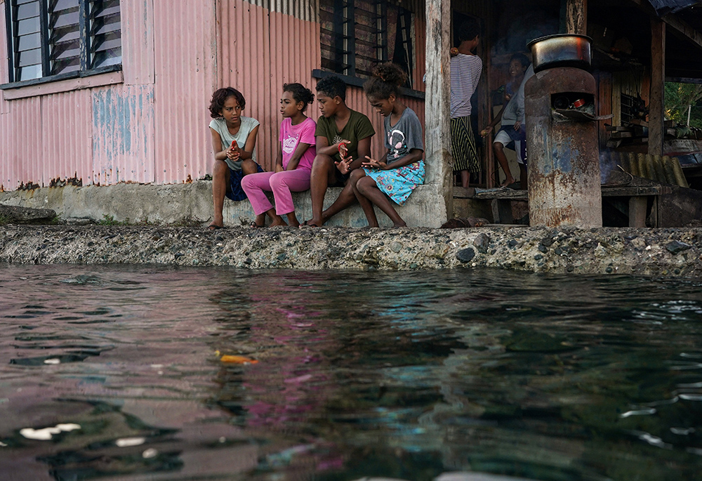 Village children pass the time in front of a home next to a flooding sea wall at high tide July 15, 2022, in Serua Village, Fiji. As the community runs out of ways to adapt to the rising Pacific Ocean, the 80 villagers face the painful decision whether to move. (CNS/Reuters/Loren Elliott)
