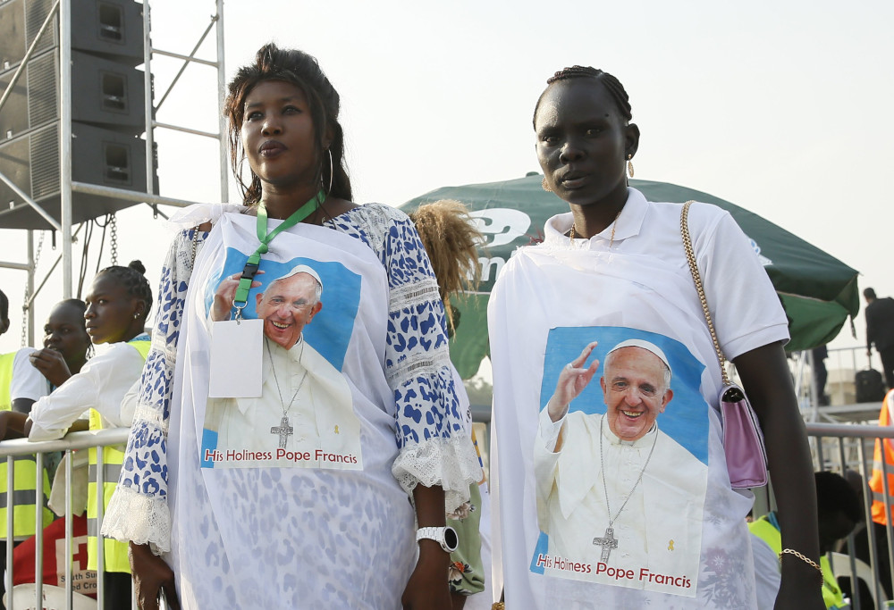 Two Black women wear wraps around their clothes with Pope Francis' face printed on them
