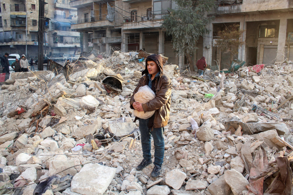 A young person stands on top of and amid concrete rubble