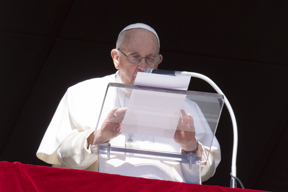 Pope Francis speaks into a microphone while holding a piece of paper over a clear lecturn