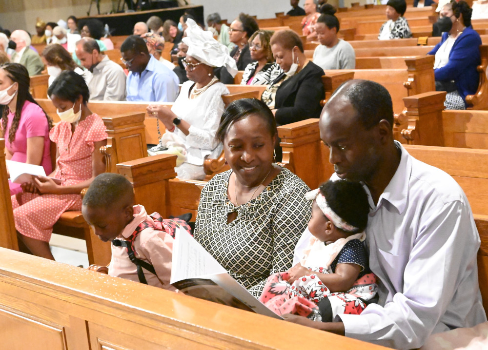 A Black family with two small children sits in a pew surrounded by other Black Catholics
