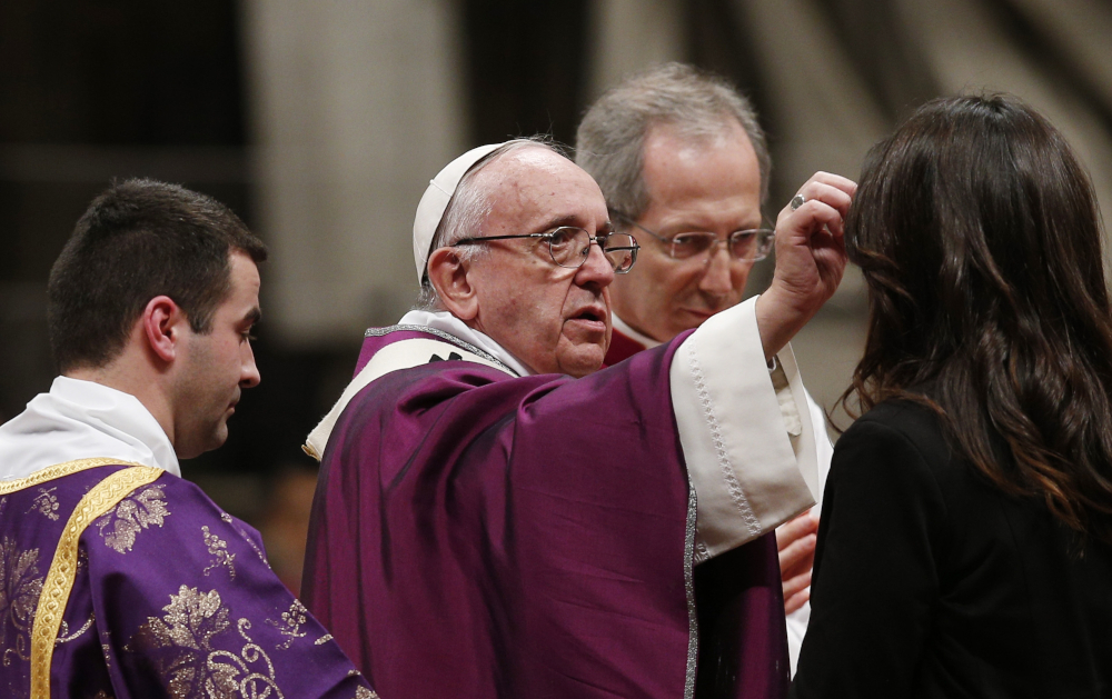 Pope Francis, wearing purple over his normal white, reaches towards a woman's forehead