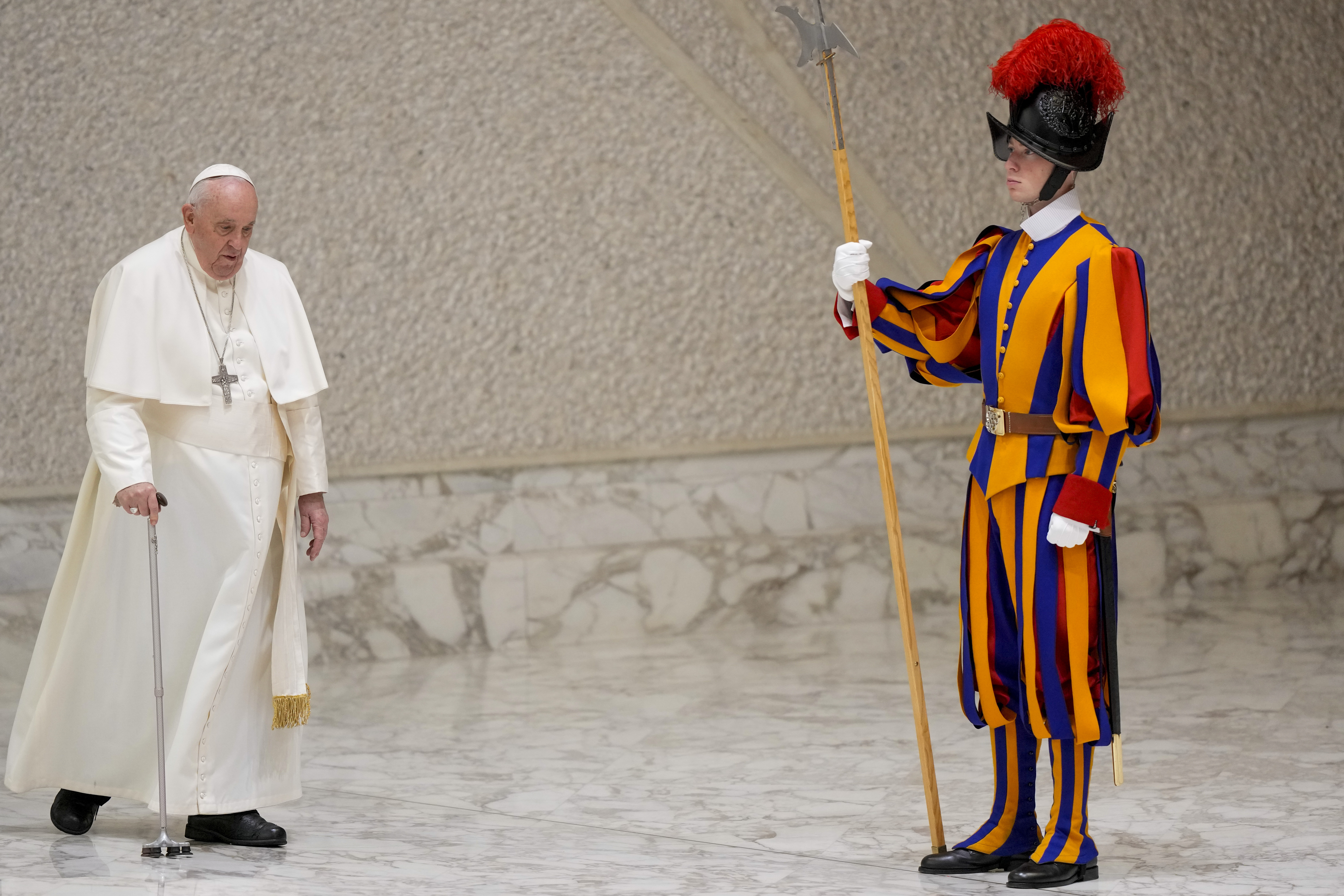 Pope Francis uses his cane to walk by a member of the Swiss Guard, who wears brightly colored stripes